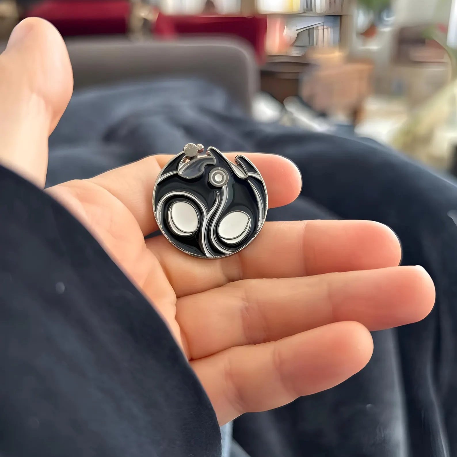 Close-up of a Void Heart Pin charm with a blurred indoor background