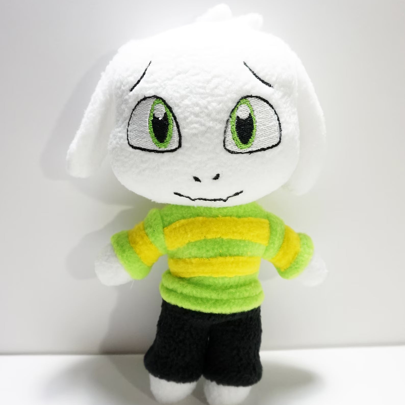 Undertale Asriel Dreemurr Plush toy with a white face, green and yellow striped shirt, and black shorts on a white background