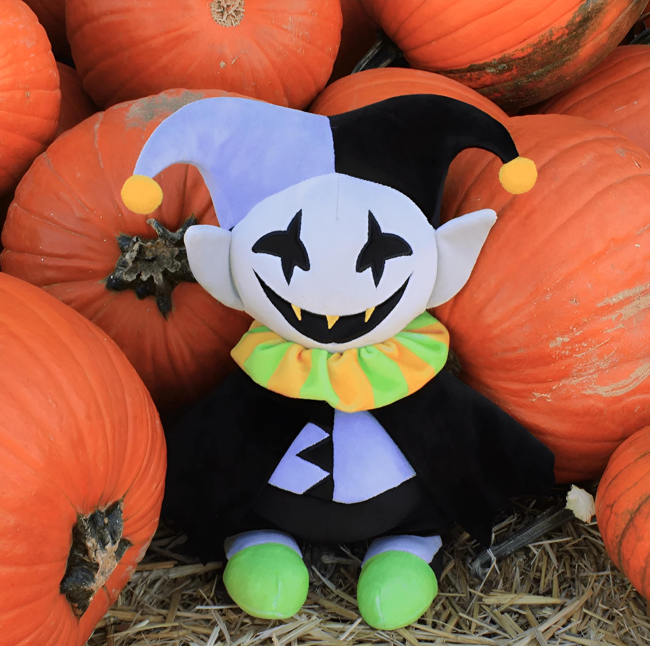 Jevil plush toy with a jester hat among pumpkins
