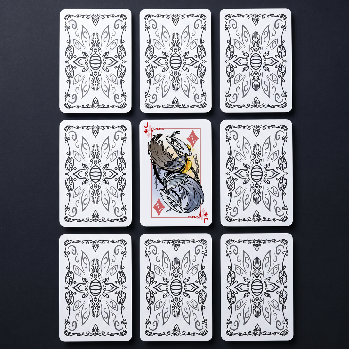 Nine playing cards from the Hollow Knight card deck laid out on a dark surface, displaying the intricate black-and-white patterned backs and the detailed Jack of Diamonds character art, fan-inspired Hollow Knight merch.