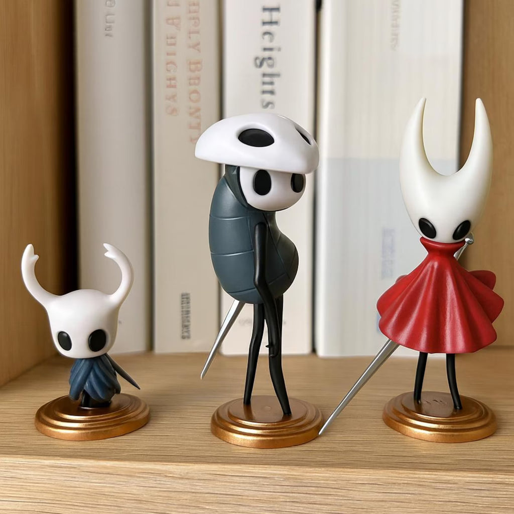Hollow Knight figurines with unique designs on a wooden surface with books in the background.