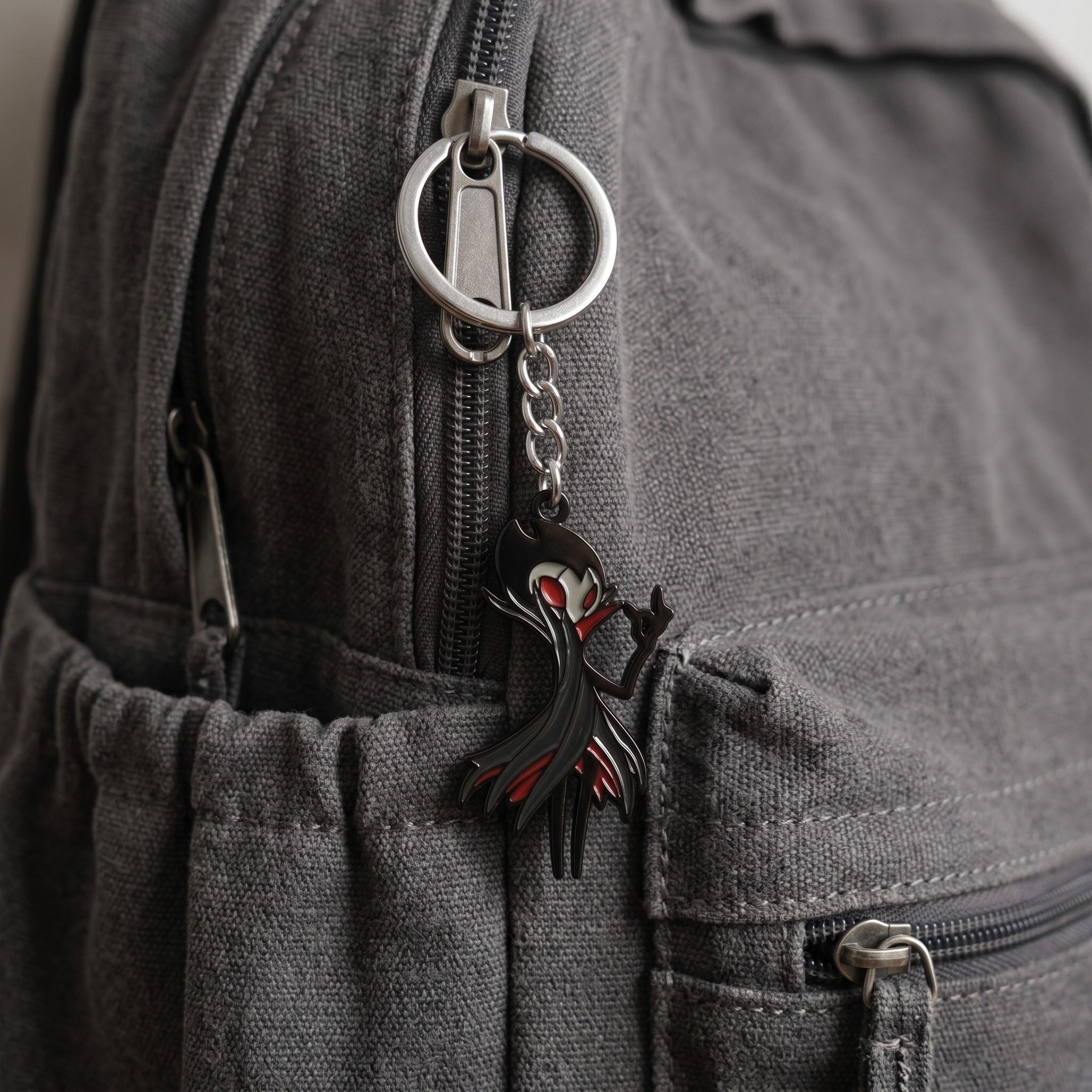 The Grimm keychain and necklace attached on a backpack, perfect fan-inspired Hollow Knight Merch.