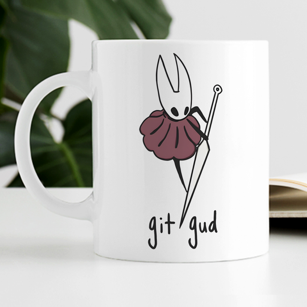 A white ceramic mug with a printed graphic of Hornet wearing a dark plum skirt and holding knitting needles, with the text 'git gud' below. The mug is set on a white surface with a blurred background showing green leaves and an open book.