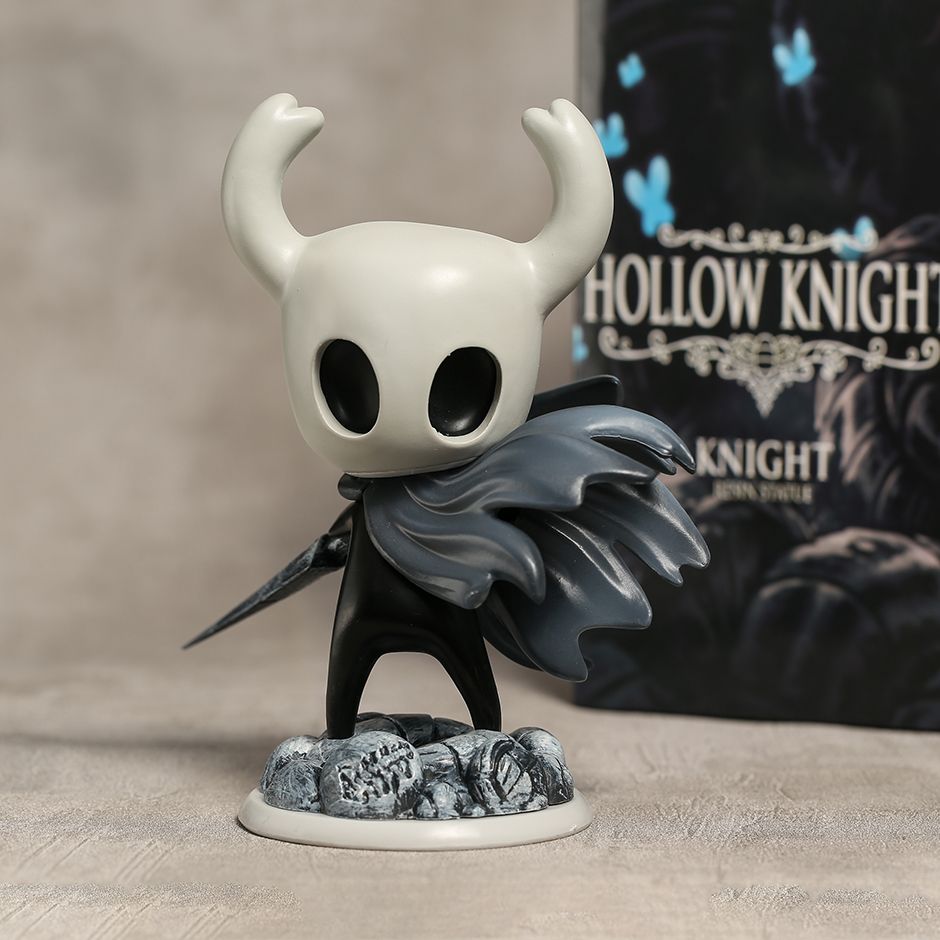 Hollow Knight figurine with a blurred 'Hollow Knight' game box in the background