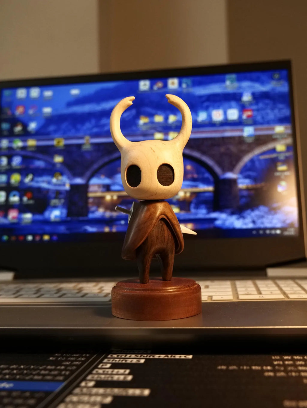 The Hollow Knight Wooden Figure displayed on a wooden desktop, emphasizing its natural look and use as Hollow Knight Merch.
