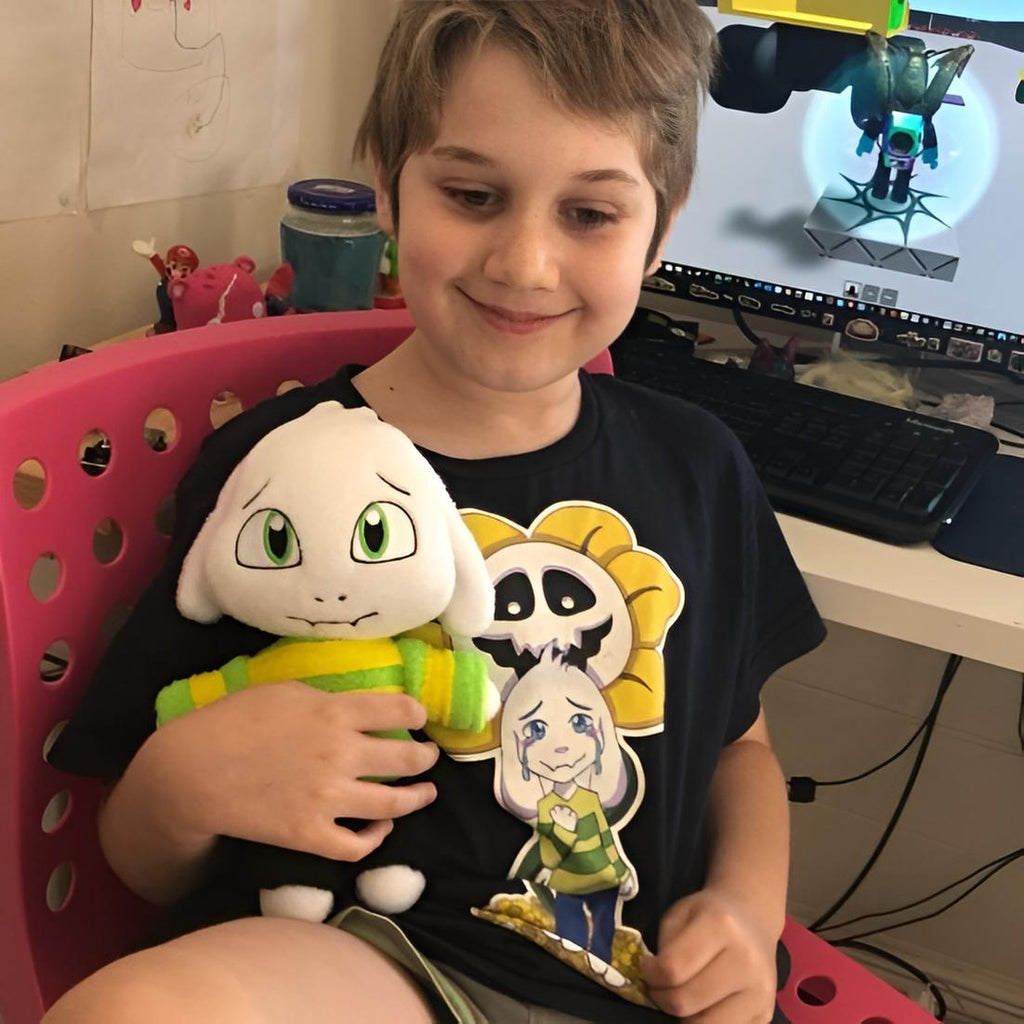 Child holding a Asriel Dreemurr plush toy in front of a computer screen